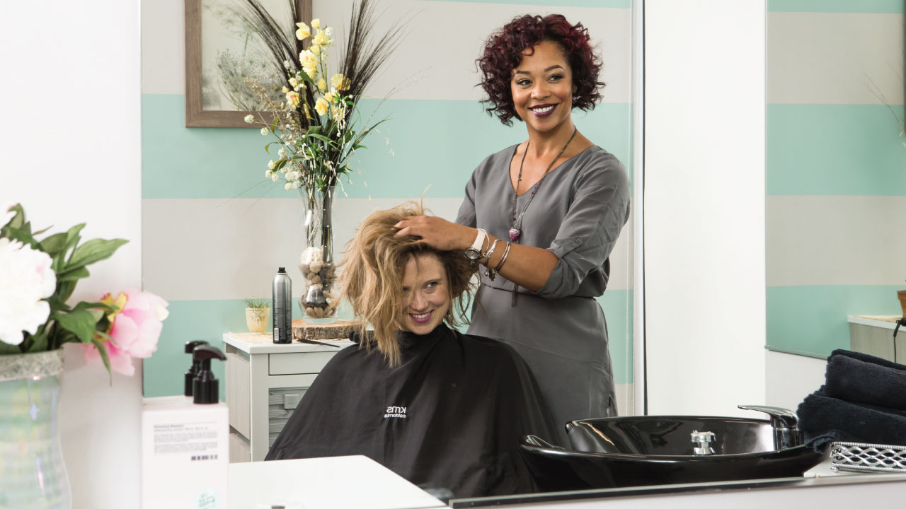 A smiling woman gets her hair styled by a proud salon professional